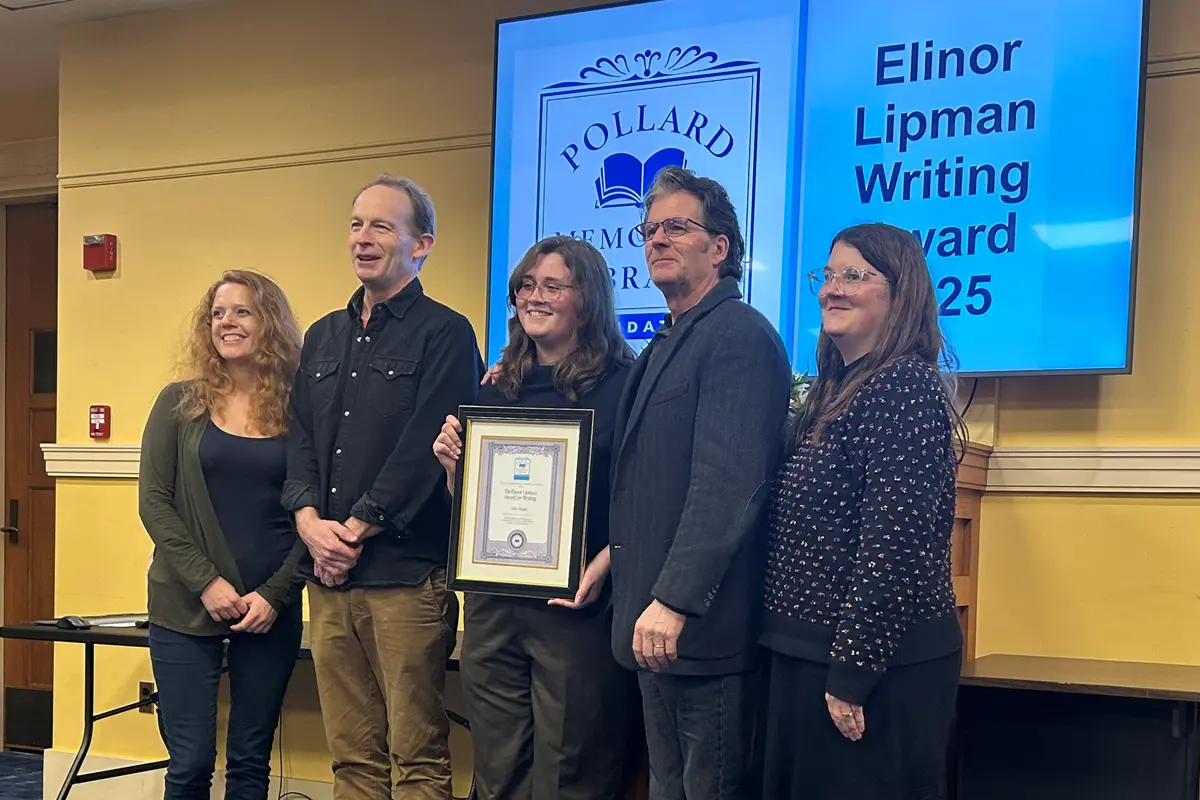 Three women and two men pose for a group photo in front of a TV screen.
