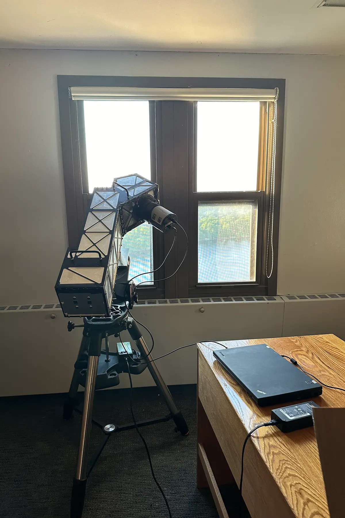 An optical spectrograph is set up facing a window in a college dorm room.