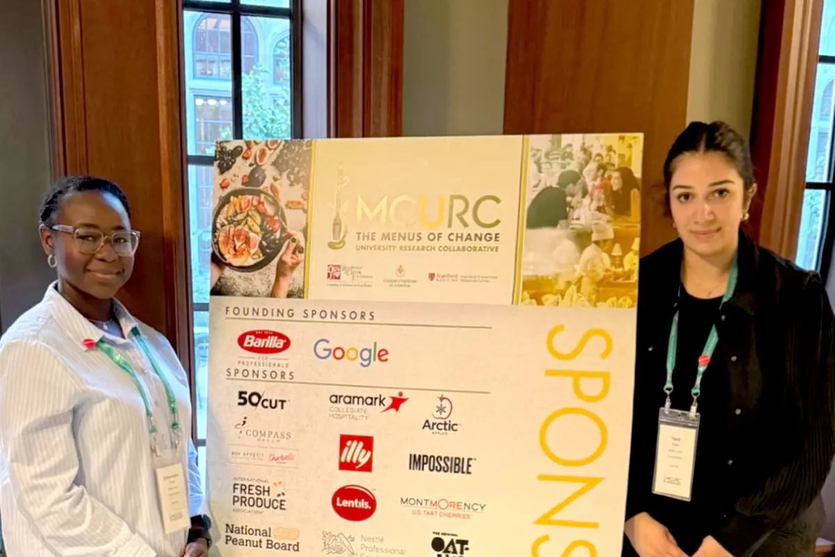 Two young women pose for a photo while standing next to a poster board.