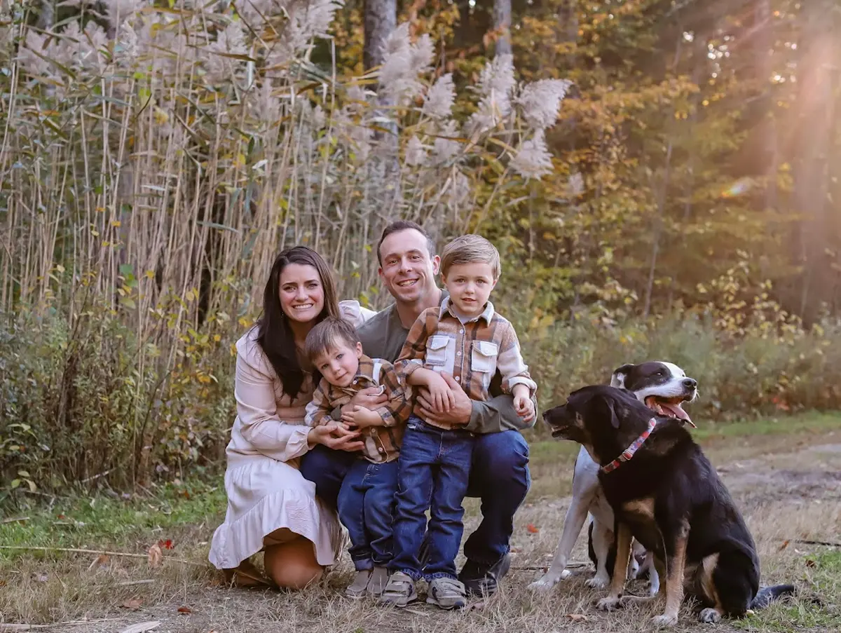 A woman and a man pose for a photo outside with two children and two dogs.