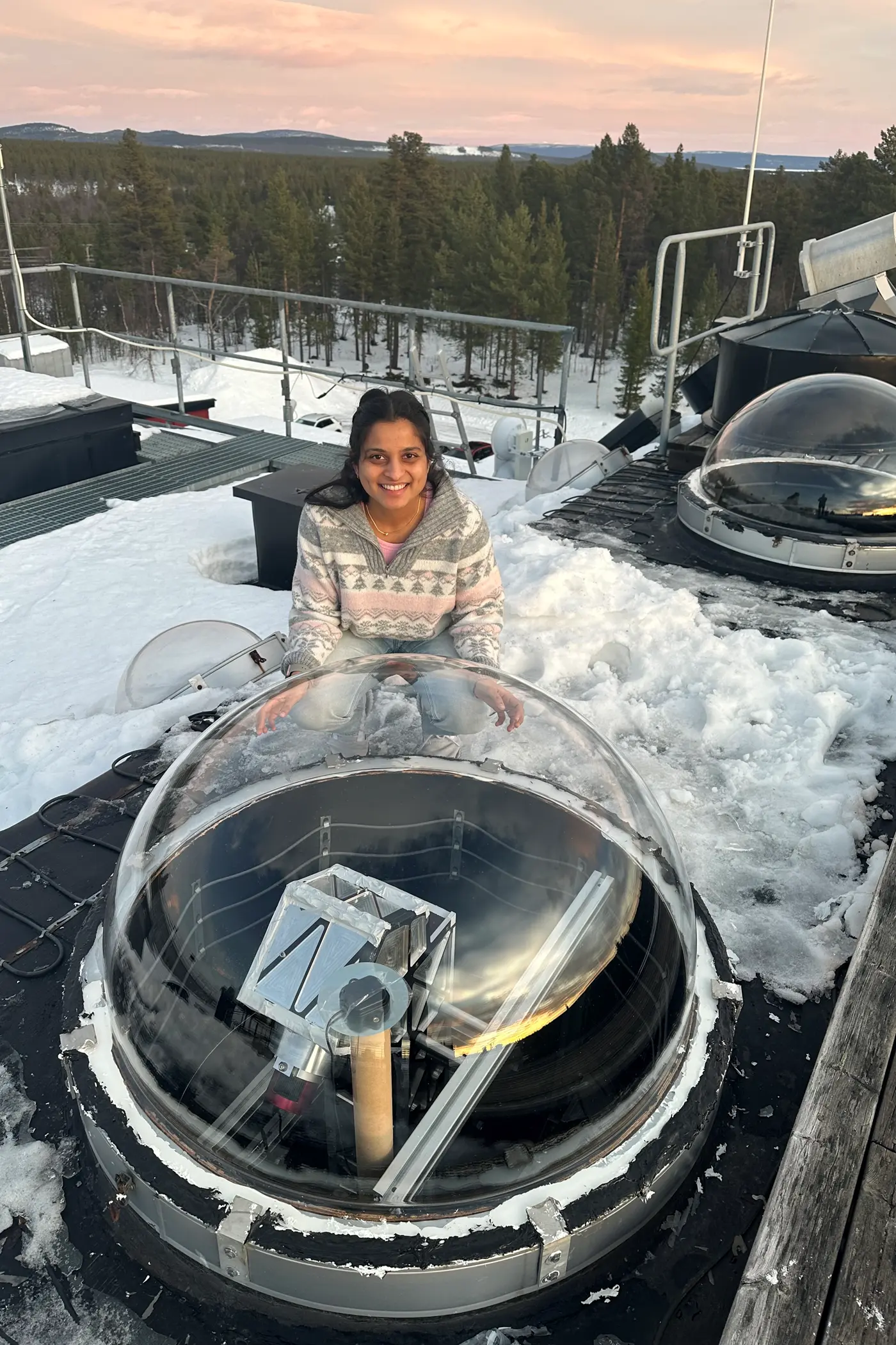 A young woman poses for a photo next to an observatory bubble on the roof of a building.
