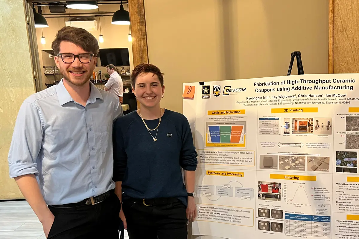 Two smiling college students pose for a photo while standing next to a research poster.