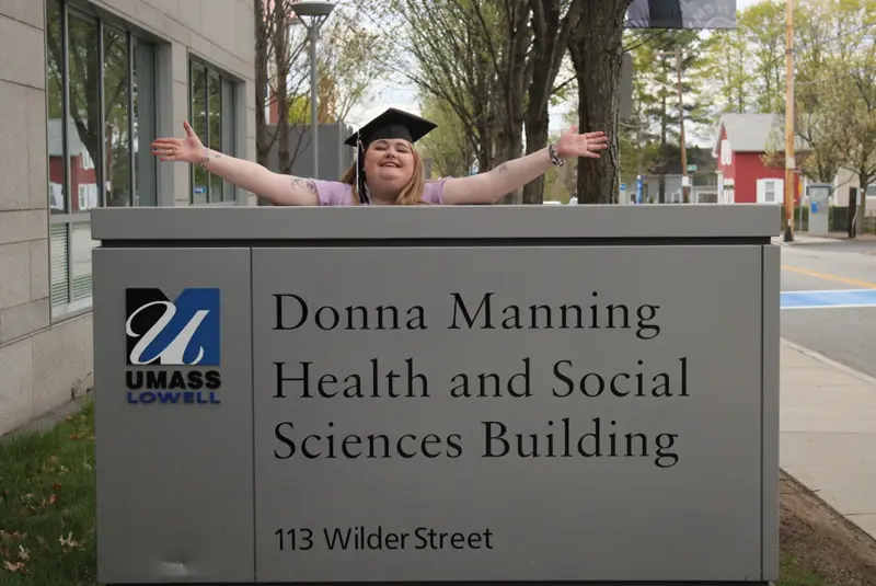 Kayla Bissonnette poses behind the sign for the UMass Lowell Donna Manning Health and Social Sciences Building.