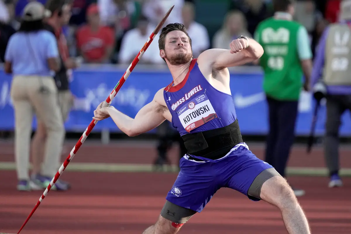 A person in a blue shirt gestures with his hand while posing for a photo at an outdoor track.