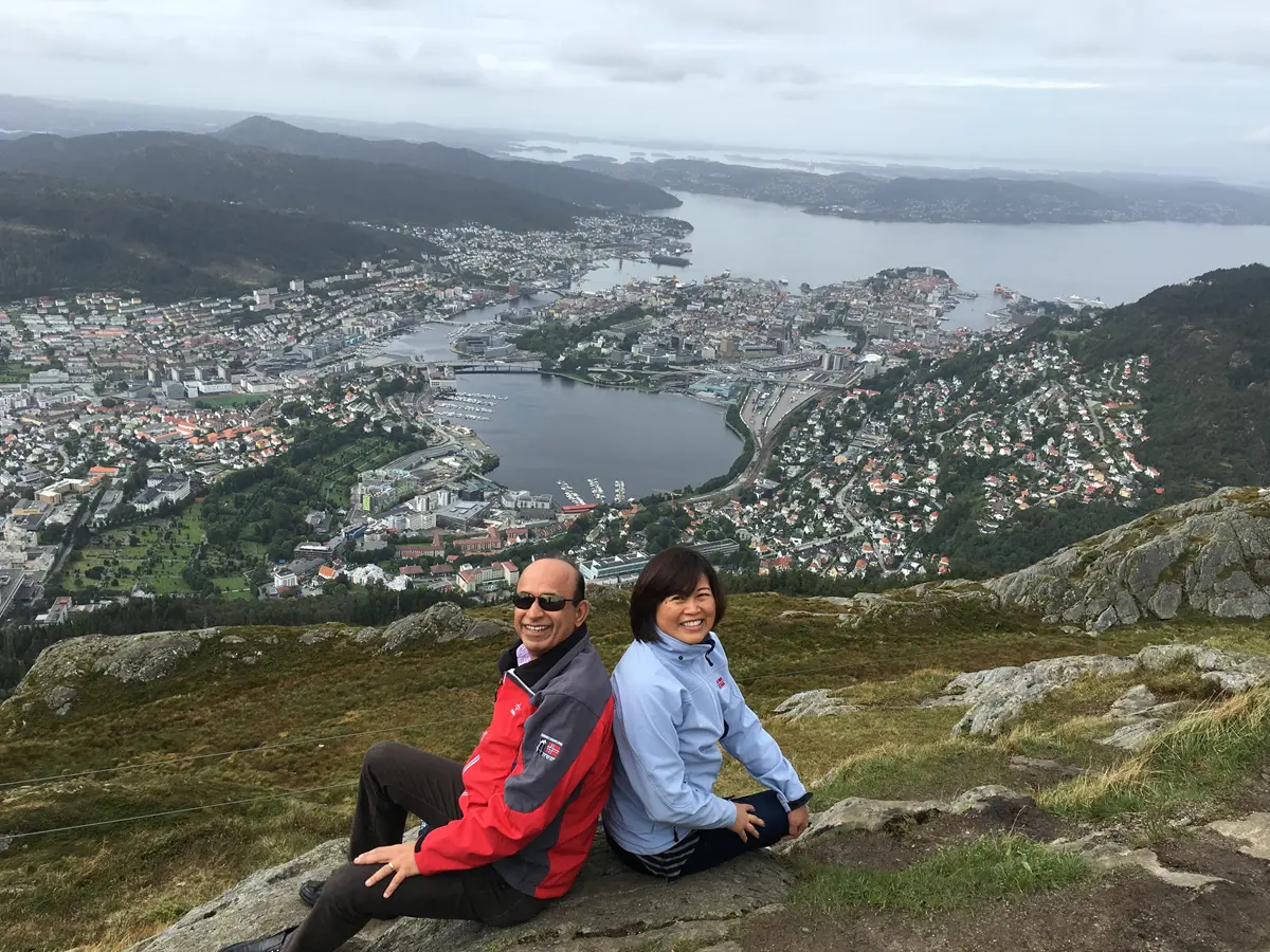 UMass Lowell alumni MK and Shuling Raheja pose on a hillside that looks over of a sprawling lakefront community
