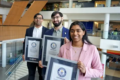 Two young men and a young woman pose for a photo in a building while holding framed certificates.