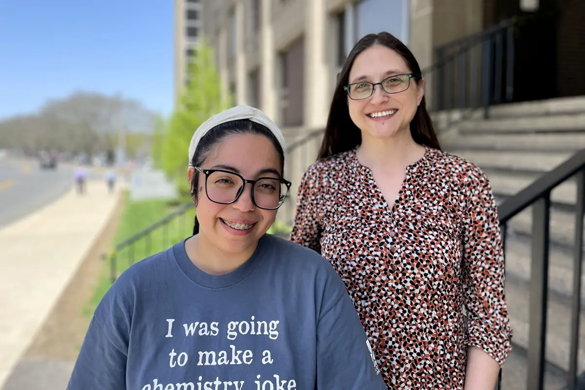 Two women wearing glasses pose for a photo while standing on the steps outside of a building.