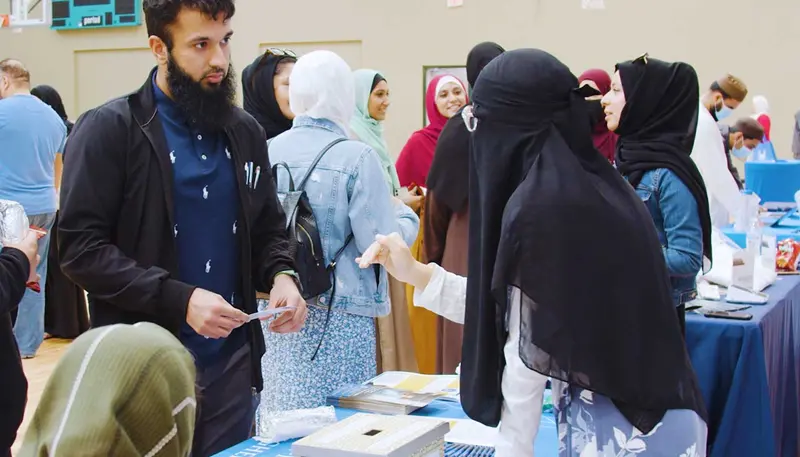 Melisa Hussain stands at a table talking with a student