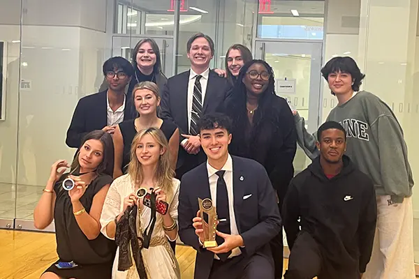 Seven UML Mock Trial students pose together and hold up team and individual awards