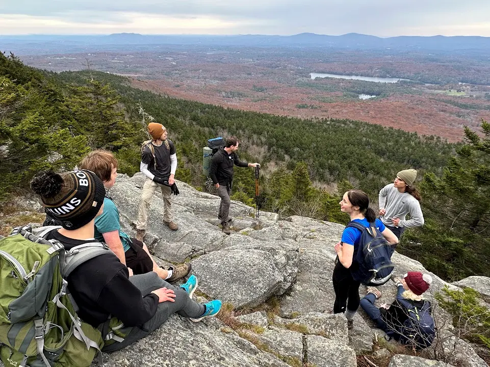 a group stands on a rocky outcrop while looking over a beautiful vista