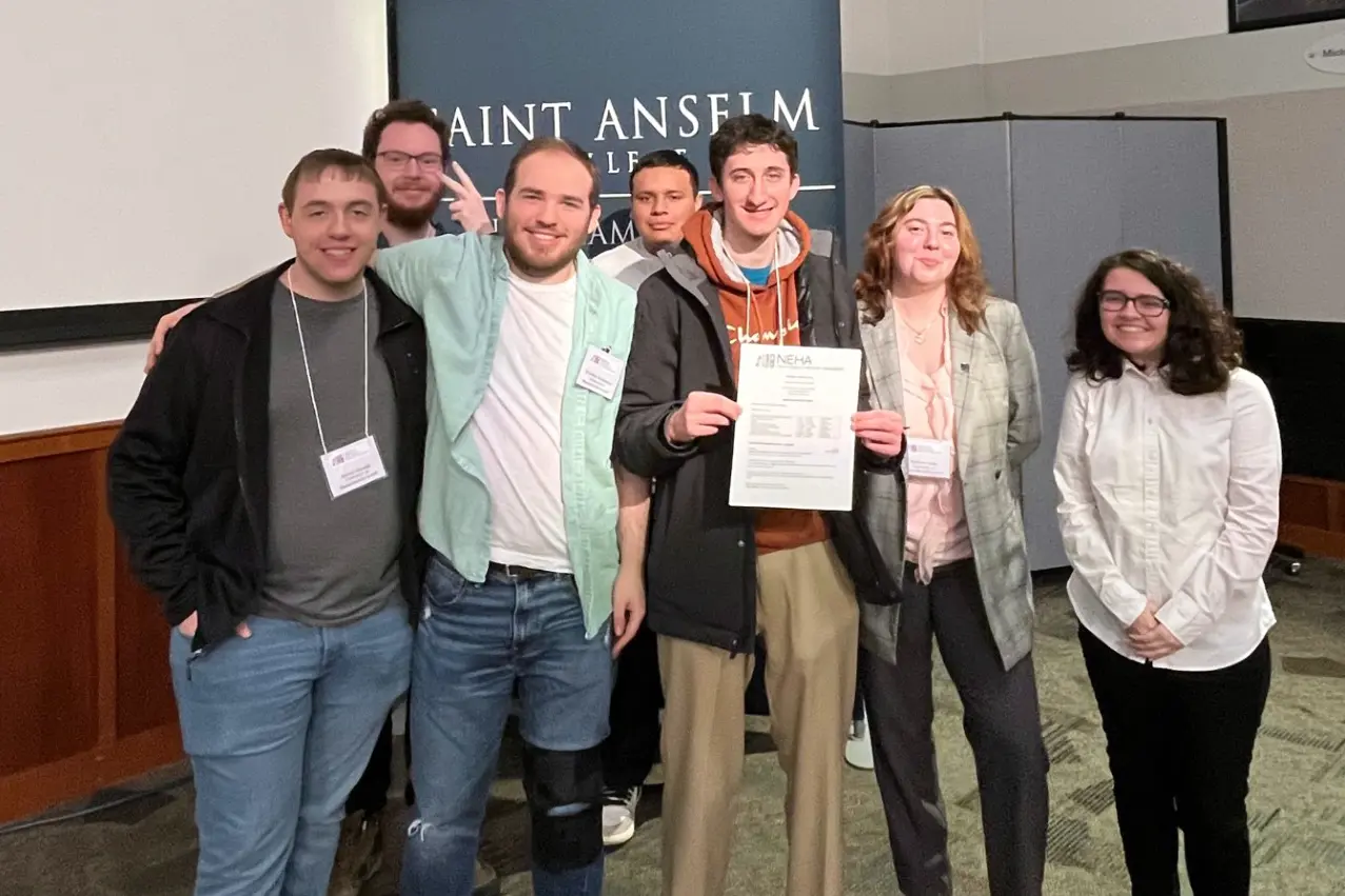 Seven people pose for a group photo. One of them is holding a piece of paper.