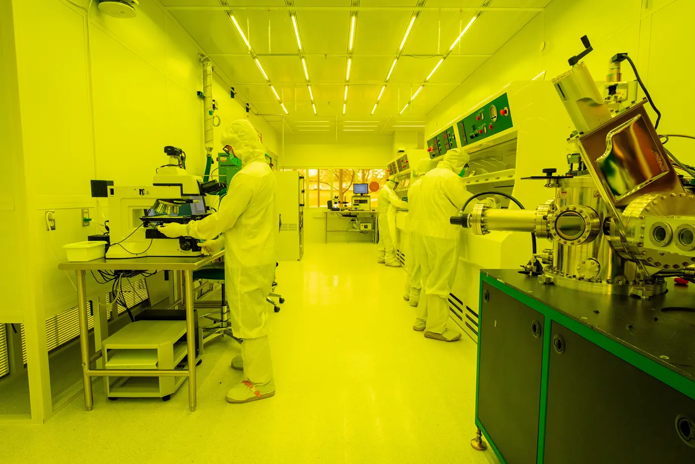 Workers in white clean room garb in a laboratory illuminated in brilliant yellow light