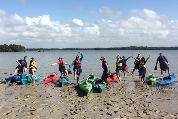 Students pose with their kayaks on the beach