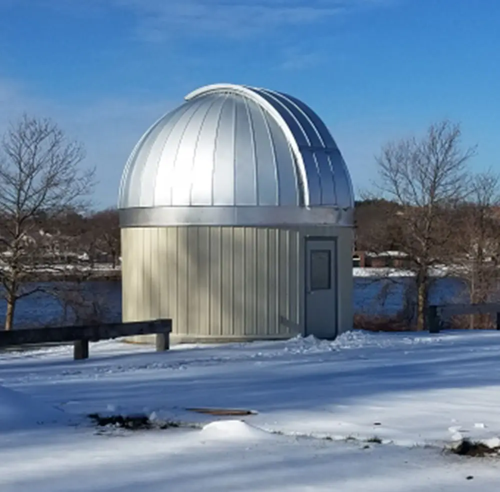 The dome has been added to the observatory. The observatory currently sits in a field of snow. The Merrimack River is visible in the background.