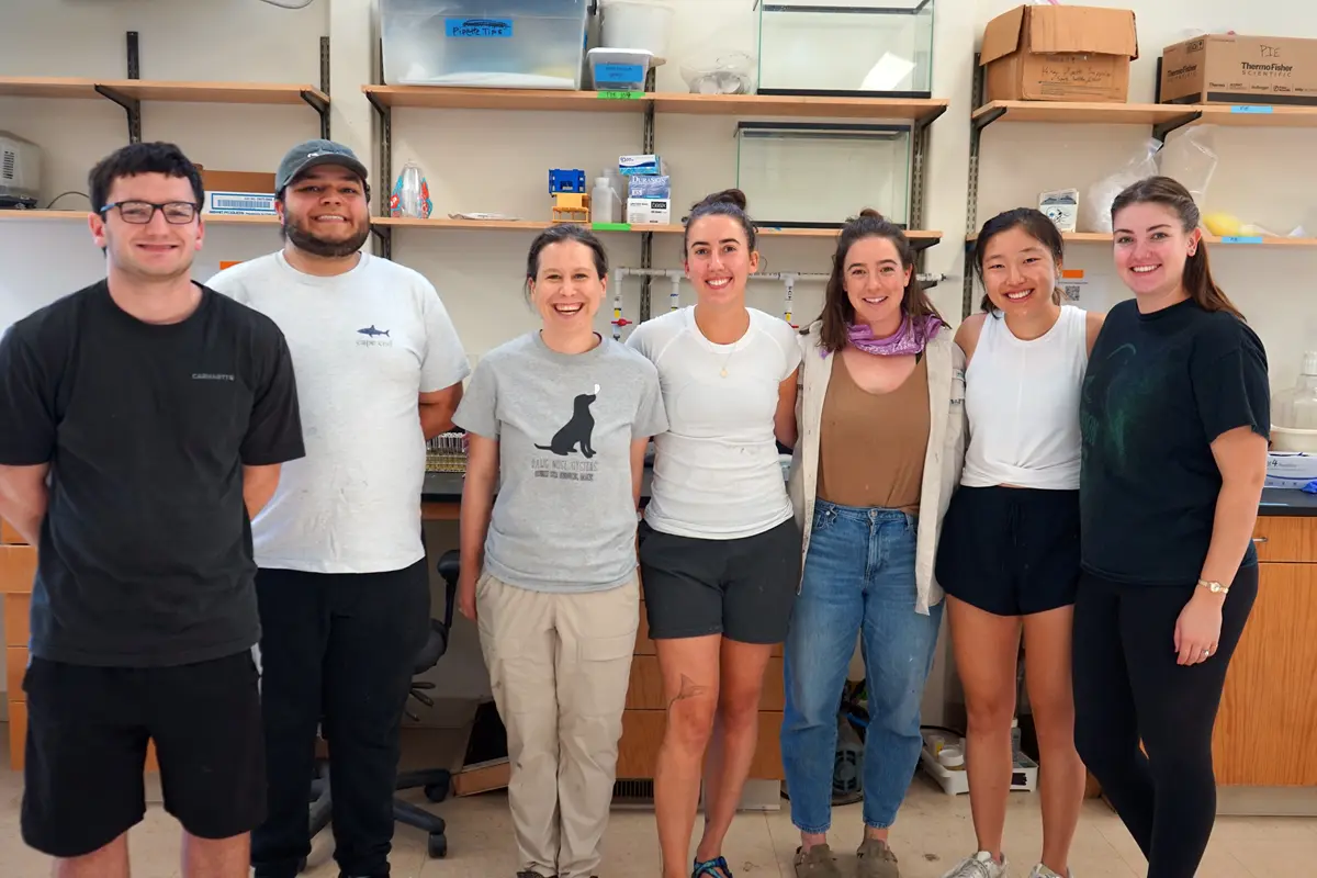 Two men and five women stand and pose for a photo in a science lab.