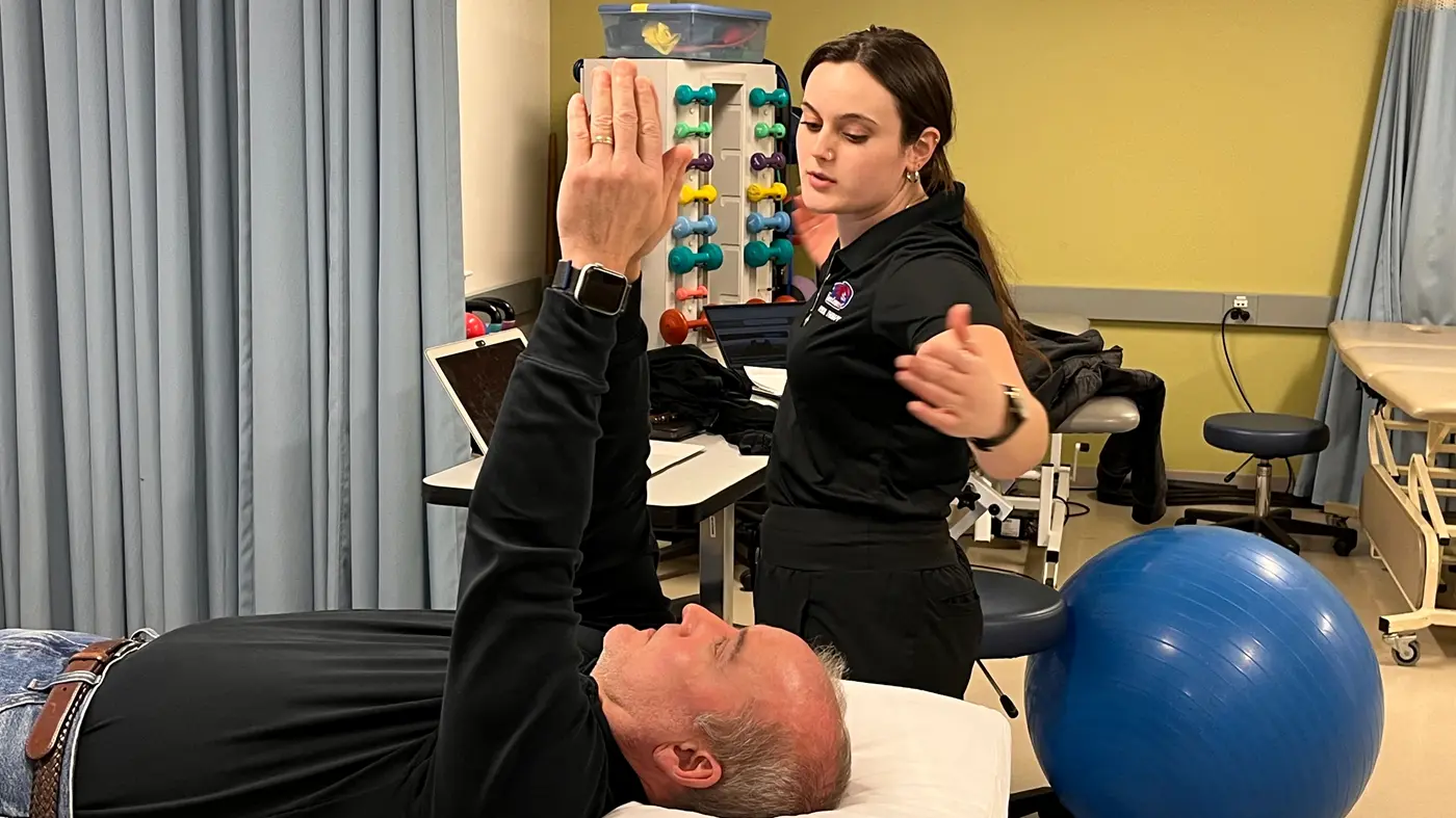 A patient lying on a table lifts his arms as he works with a student in UMass Lowell's physical therapy clinic.