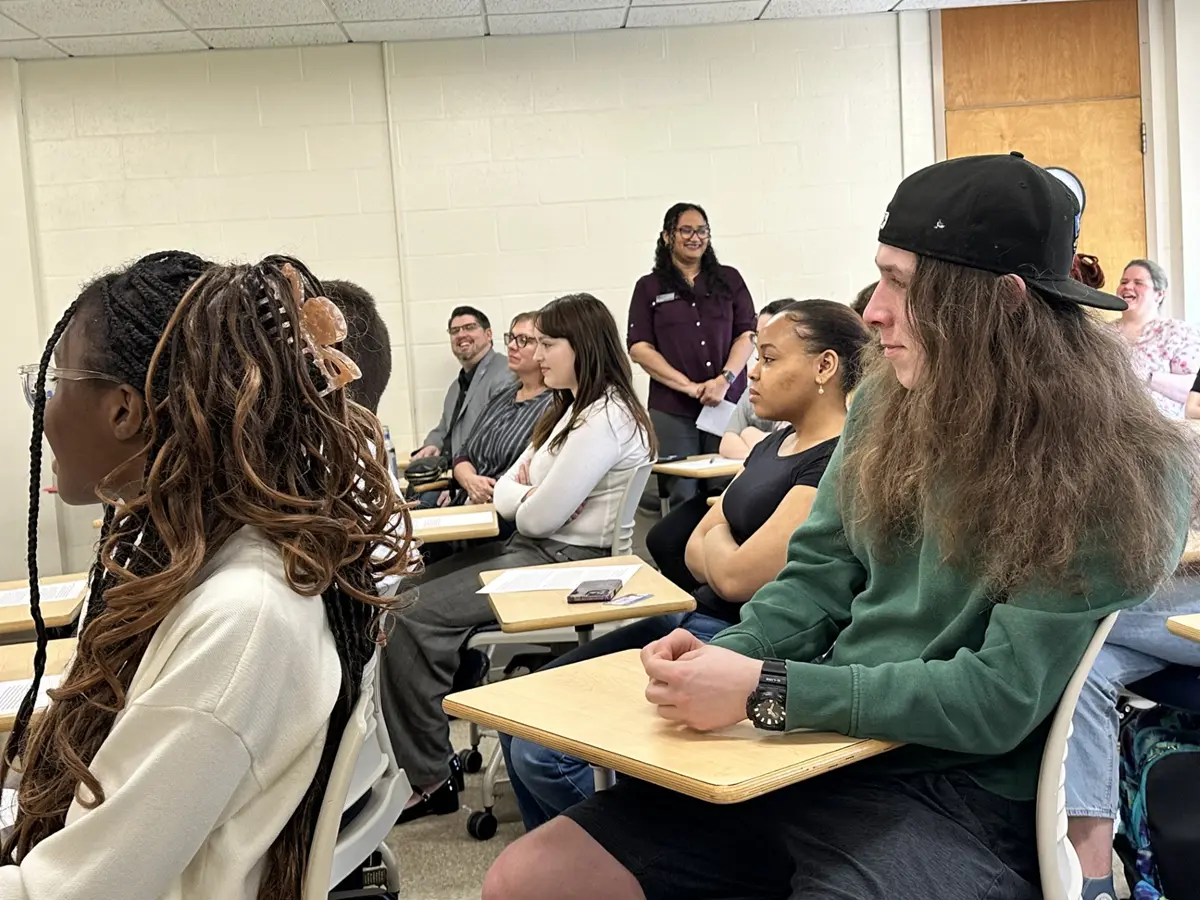 Students sit at desks and listen, facing left