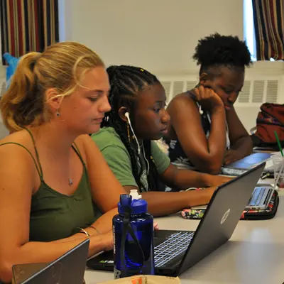 Three young people work on laptops at a table.
