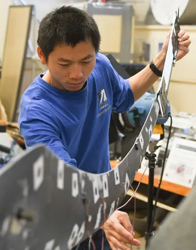 Student inspects test wind turbine blade in the research lab. The STRUCTURAL DYNAMICS & ACOUSTIC SYSTEMS LAB's research is related to analytical and experimental problems in the areas of structural and acoustic systems. The main thrust of the SDASL is to develop, employ and improve techniques to solve these problems using analytical approaches that are verified through experimental techniques.