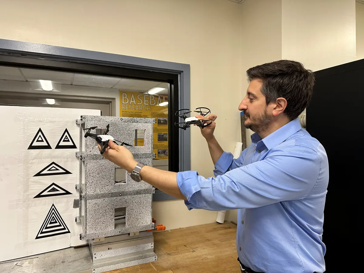 Mechanical Engineering Asst. Prof. Alessandro Sabato holds two small drones near a speckled surface in his lab