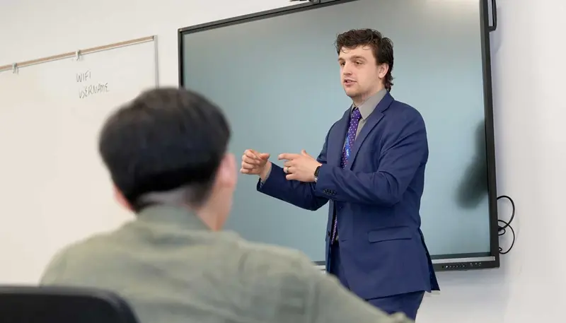Sam DeLap delivers a presentation in front of a screen.