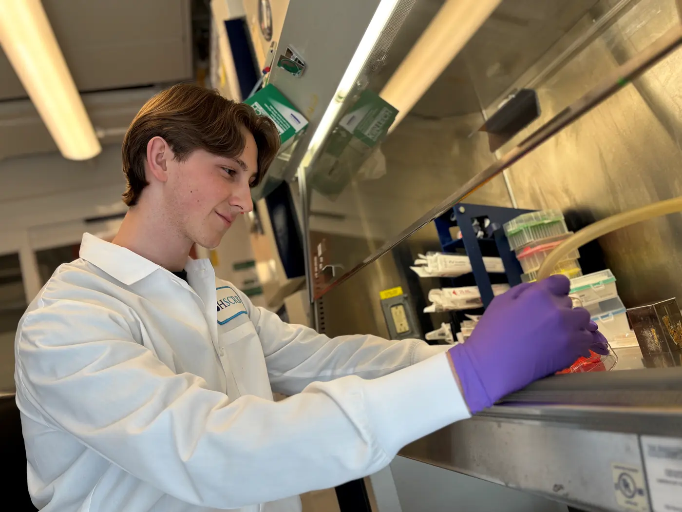 Sean Simonini dressed in a white lab coat works on a petri dish in a lab