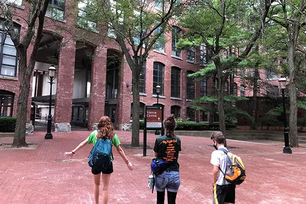 Three people walk in a brick plaza toward a sign that says "visitor center"