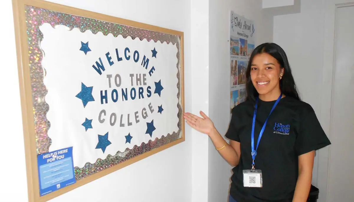 Suhani Karki points to a bulletin board that say "Welcome to the Honors College."