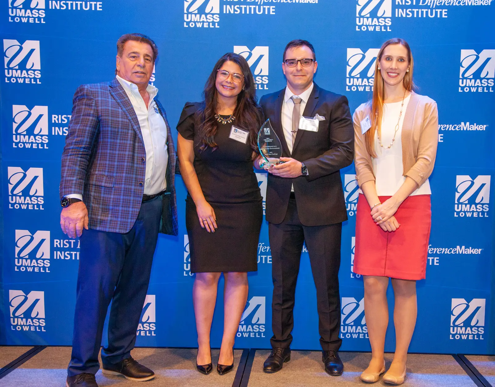 Ariel Pena-Martinez, computer engineering graduate student, and Grissel Cervantes-Jaramillo from the ThermoEXA team holding an award pose with Brian Rist and Holly Lalos of Difference Makers against a blue UMass Lowell backdrop.