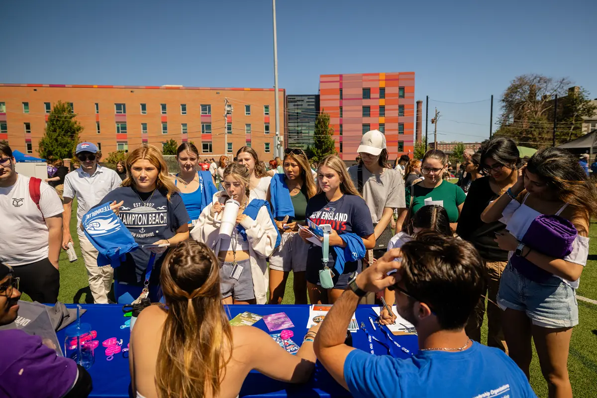 A group of students talk to people seated at a table during an outdoor engagement fair.
