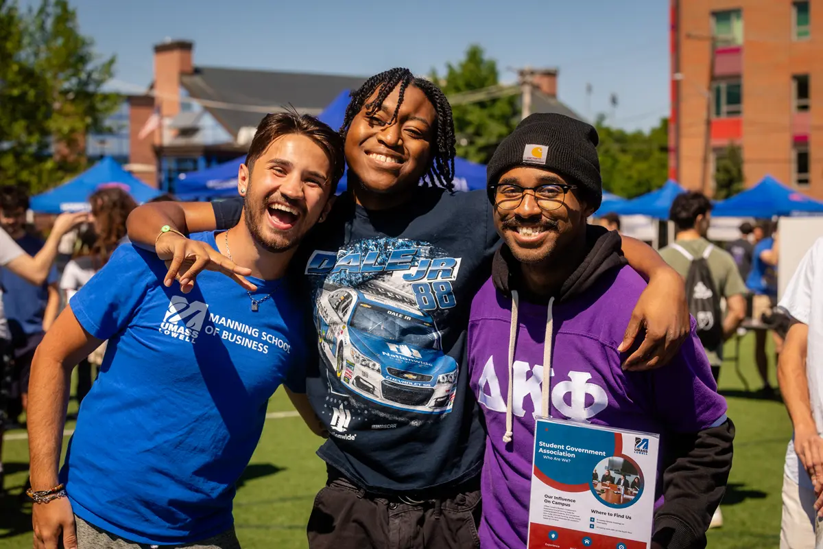 Three students smile and pose for a photo while standing outside at an engagement fair.