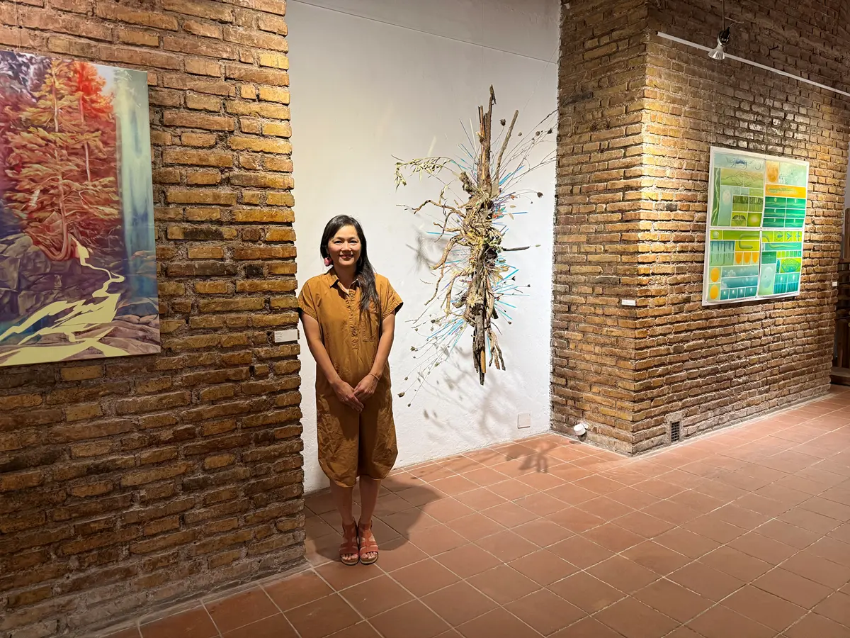 A woman stands next to a sculpture made of organic materials in an art gallery.