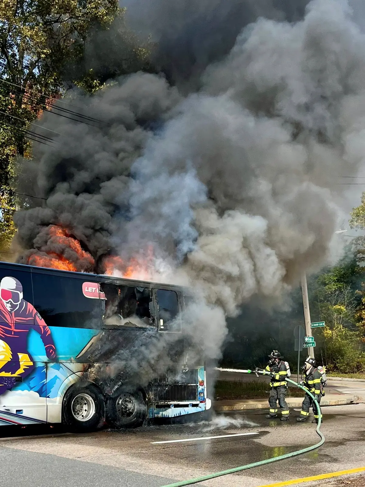 Two firefighters spray water on a burning charter bus.