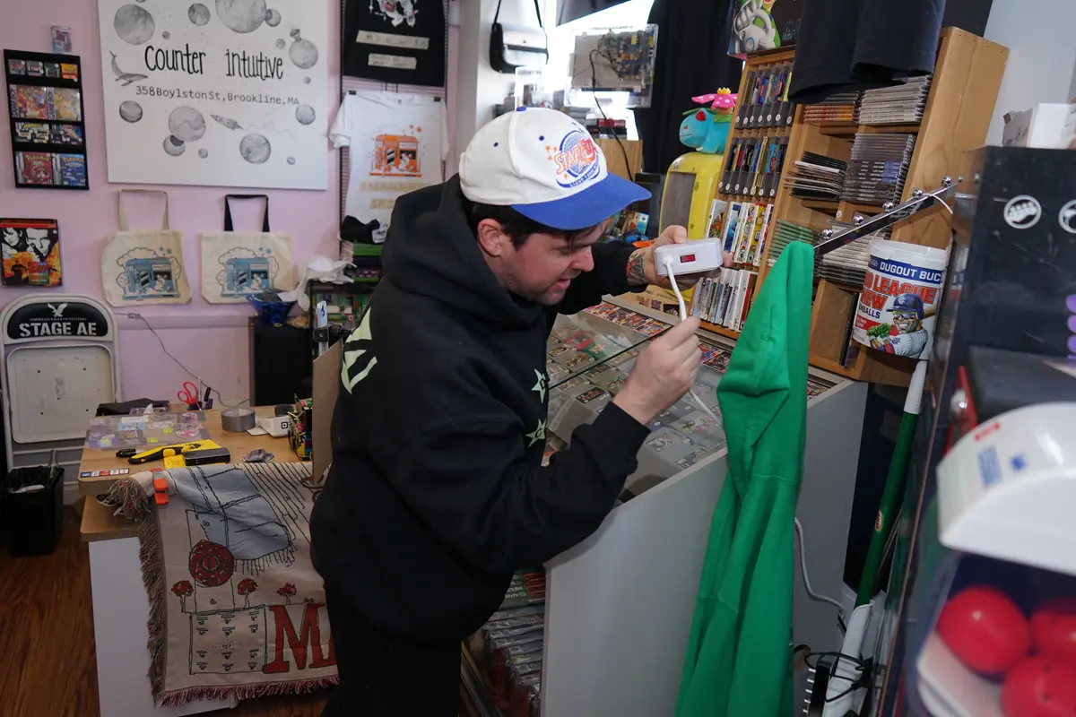 A young man in a baseball cap hooks up electronic equipment inside a record store.
