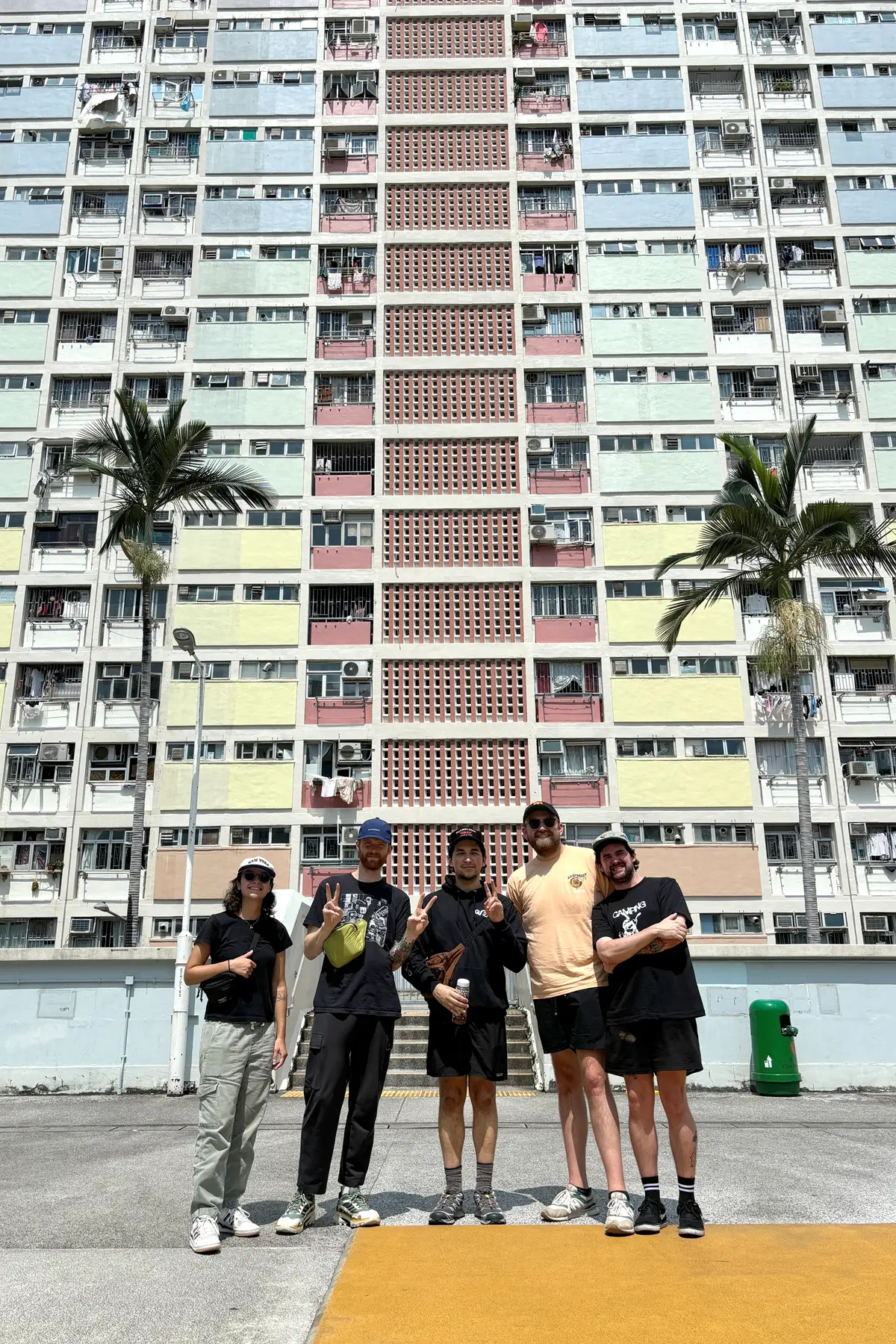 Five people pose for a photo while standing in front of a pastel apartment building and two palm trees.