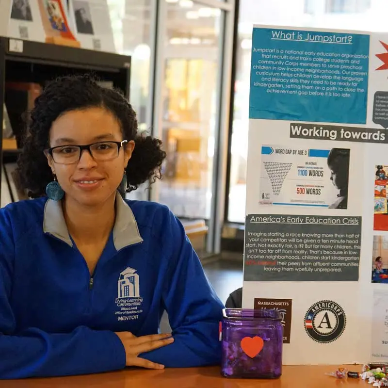 Emily Crespo sits at a table with a Jumpstart poster.