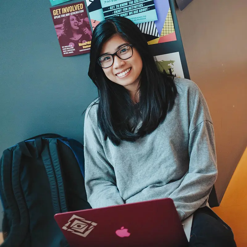 Student with glasses sitting with backpack and laptop computer.