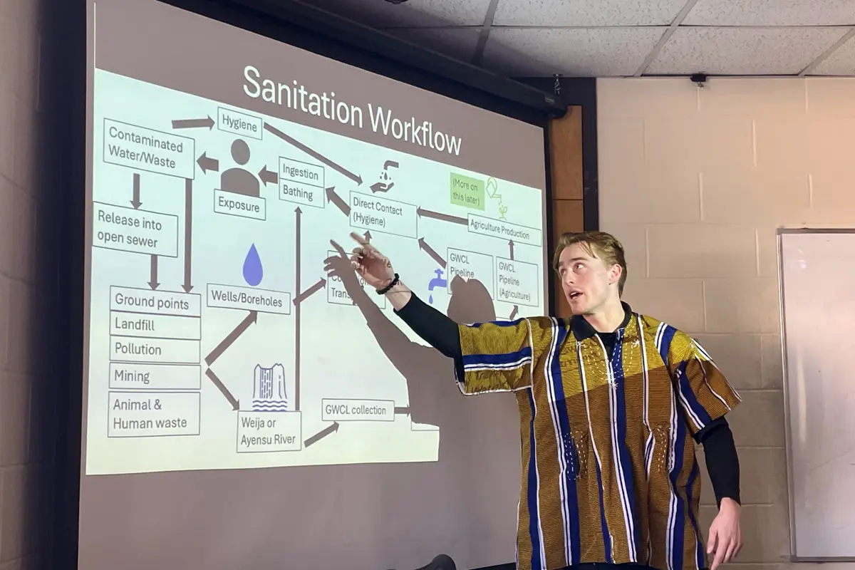 A college student points at a project screen while making a presentation.