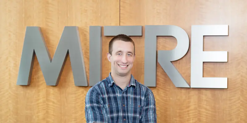 John Kilgo smiling in front of MITRE signage