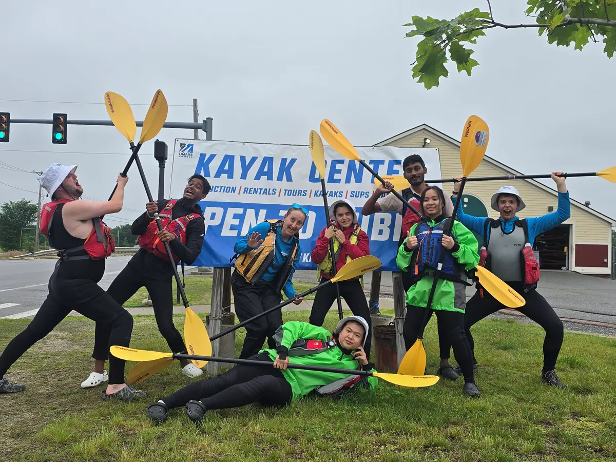 a group of kayak center staff stand in front of the sign making silly faces and poses