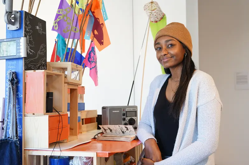 Lana Bashir sits at a colorful desk with a notebook, various equipment and flags.