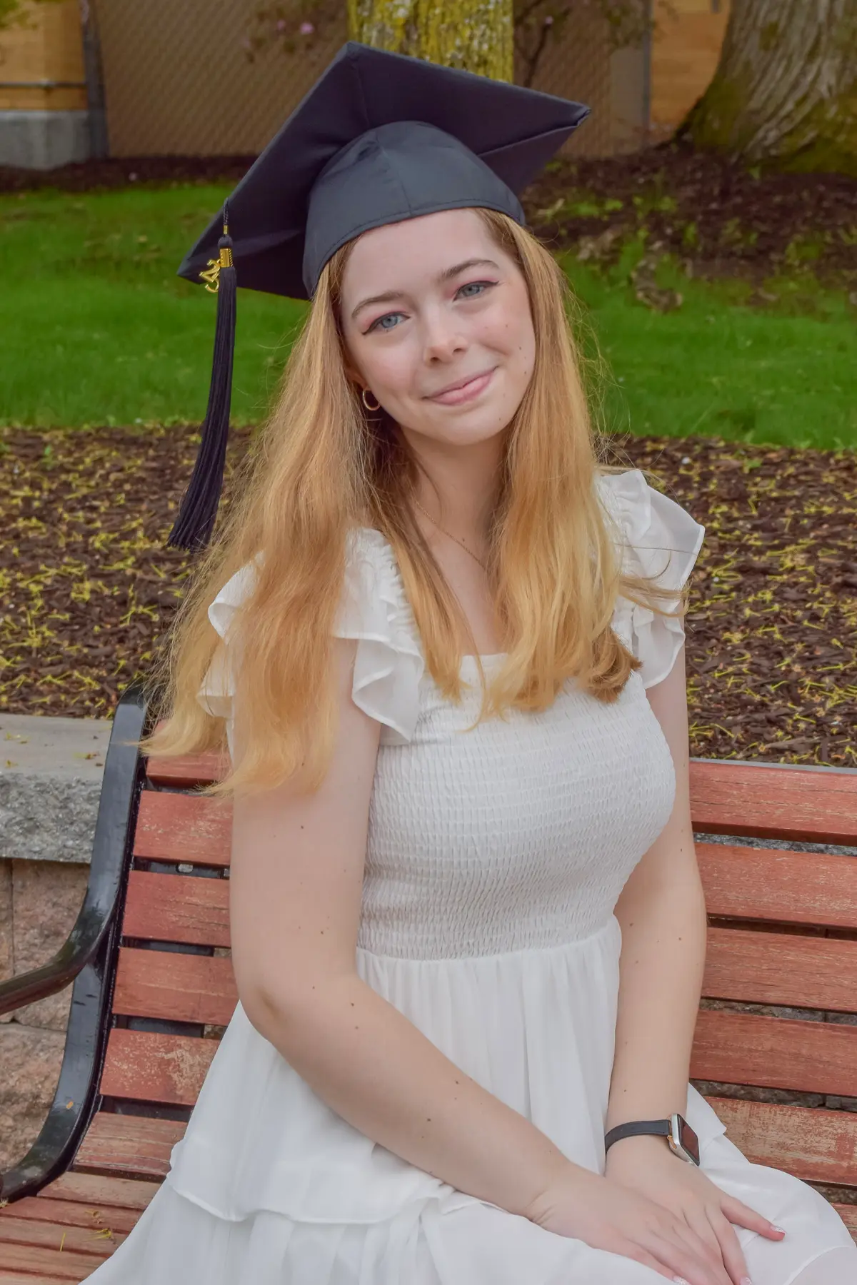 A young woman in a white dress and graduation cap poses for a photo.