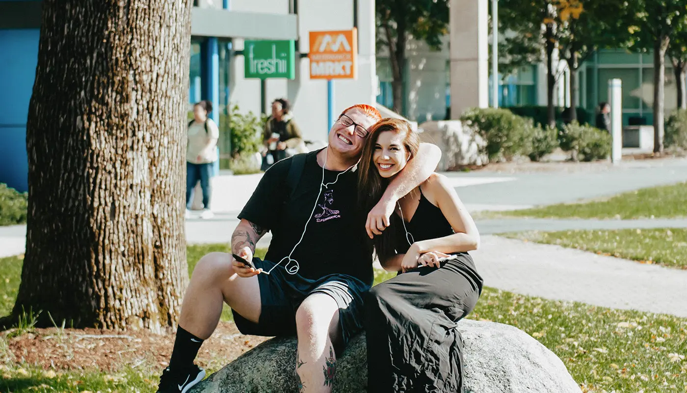 male and female students sitting on a rock on UMass Lowell's south campus