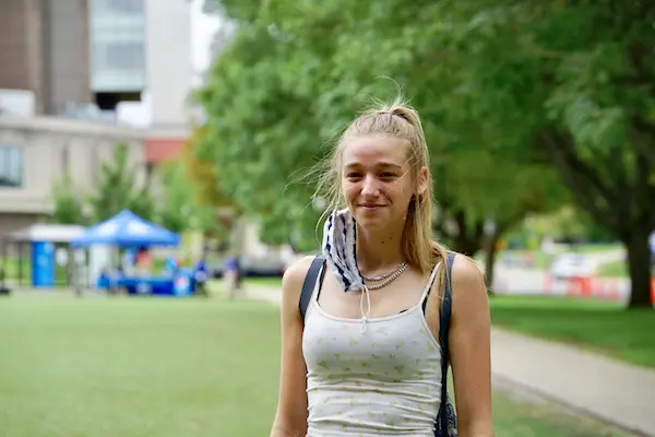 A female student with blonde hair poses for a photo outside