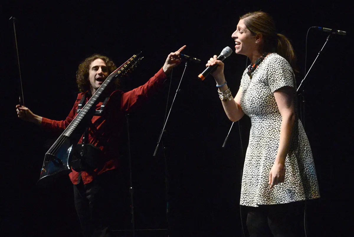 Music students performing on stage. Male with instrument and bow, female singing.