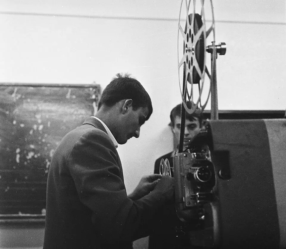 Black and white photo of people loading an old film projector.