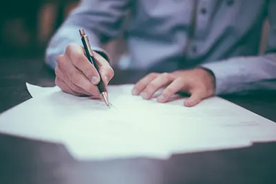 Purchasing-Office Paper: a person is seen writing on a few office papers laid out on their desk.