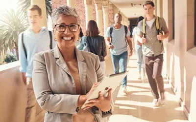 Smiling professor with tablet computer with students walking past in the background