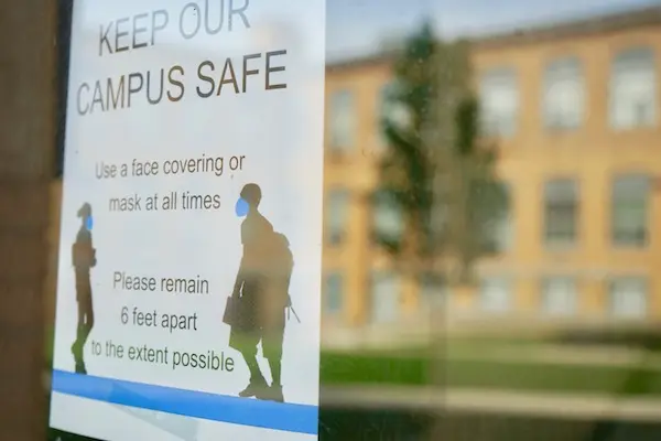 a sign about masks and social distancing on a door on campus