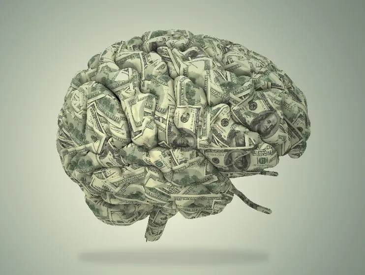 A photo of a human brain sculpted out of $100 bills on a green background.